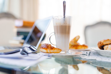 Home office, ideal working environment with breakfast. Luxury interior, glass table, reflection, notebook, eyeglasses, mobile phone and blurred background. Wellbeing at work.
