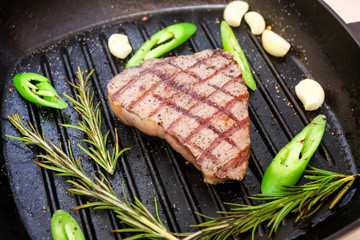 Roast beef steak on a grill pan with rosemary, garlic and green hot pepper.