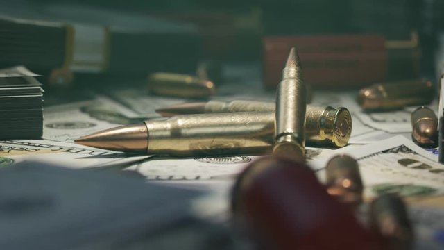 Few ammo bullets on a table in the dark covered with countless dollar bills.4KHD
