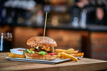 Hamburger with wooden spike served with french fries and tomato sauce. Blurred counter bar in the background. Copy space