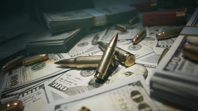 Few ammo bullets on a table in the dark covered with countless dollar bills.4KHD