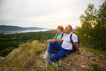 Fototapeta na wymiar elderly couple with backpacks sits on the mountain. Senior couple walking in nature. travel tourism concept