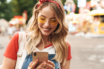 Young cheery blonde woman in amusement park using mobile phone.
