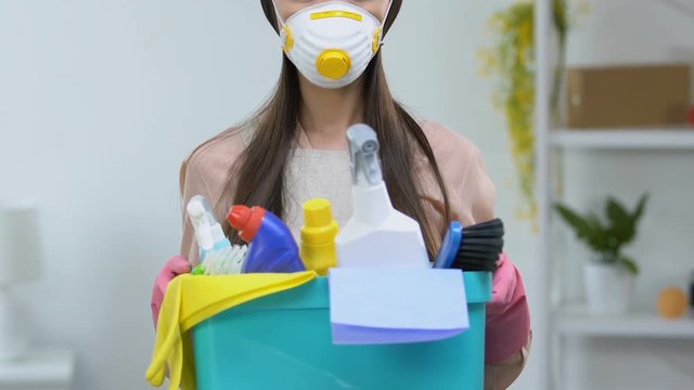 Housewife in respirator holding basket with detergents, dangerous chemicals