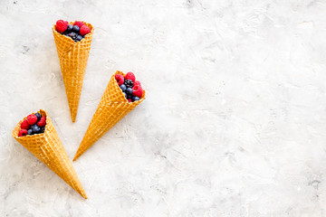 Fresh berries in waffle cones on light stone background top view mock up