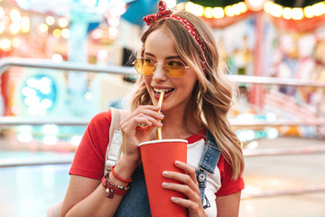 Image of attractive charming woman drinking soda beverage from paper cup while walking in amusement...