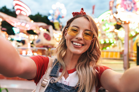 Image of young blonde woman laughing and taking selfie photo at amusement park