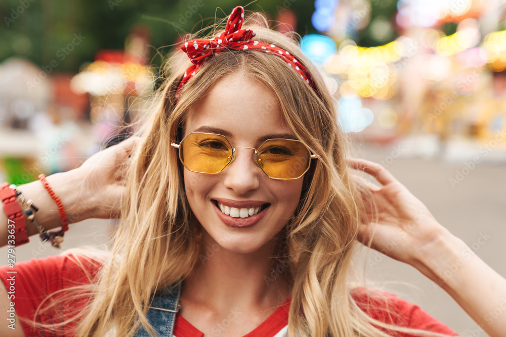 Wall mural Image of caucasian blonde woman smiling and walking in front of colorful carousel at amusement park