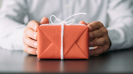 Goods delivery service. Closeup of red gift box in business man hands. Copy space.