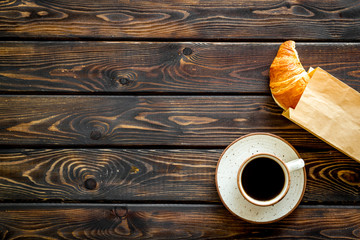 Breakfast with croissant in paper bag and cup of coffee on wooden background top view mock up