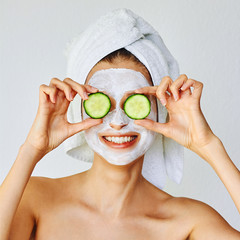 Beautiful young woman with facial mask on her face holding slices of cucumber. Skin care and...