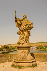 Obraz premium Ancient statue of Saint Nepomuk at old city bridge illuminated with golden sun at sunset in Wurzburg, Germany, summer time