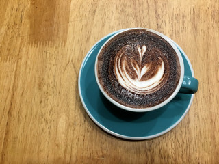 Hot dark chocolate in blue cup on wooden table background. Art of milk foam drawing like white leaf on dark brown melt chocolate top view.