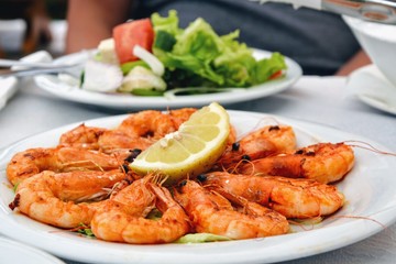 Delicious roasted shrimps with lemon on the plate. Fried seafood around quarter of a lemon on the restaurant table. Close up