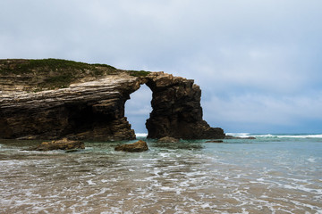 Natural arch in rock in Las Catedrales beach (beach of the cathedrals) near Ribadeo, Galicia, Spain. A Natural Monument known for its rock formations, arches and caves, only appreciable at low tide