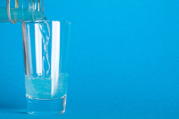 Blue carbonated liquid is poured into a glass from a bottle on a blue background