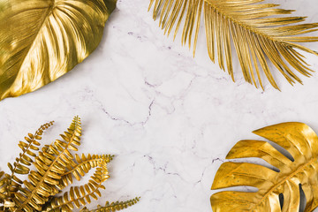 Creative layout made of golden tropical leaves and palms on white marble texture background....