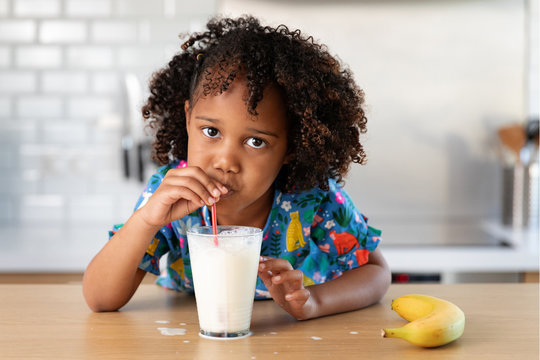 Young girl with afro hair blowing bubbles in a glass of milk
