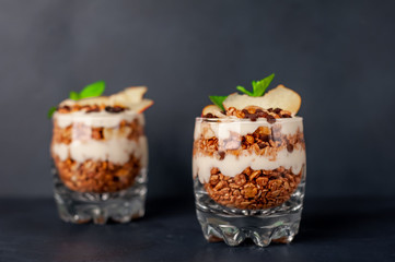  two muesli parfaits, yogurt, fresh peach, banana chips, mint, healthy breakfast on a stone background