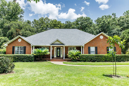 Front view of red brick house in the suburbs with a spacious lawn and trees with lots of curb appeal