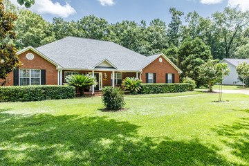 Fototapeta na wymiar Front view of red brick house in the suburbs with a spacious lawn and trees with lots of curb appeal