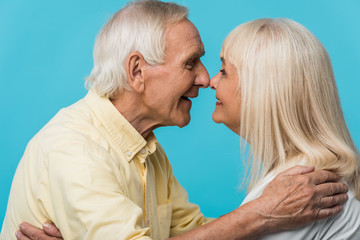 happy retired man looking at cheerful wife and smiling isolated on blue