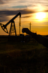 A man holding a flask of oil. Oil rigs in the background. Oil production in Russia. Sunset.