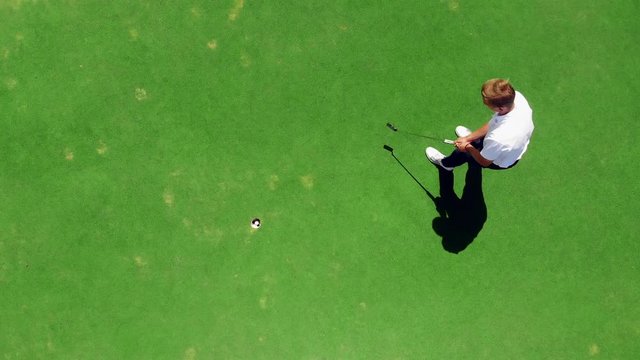 Young golfer practices on a course, hitting a ball into a hole.