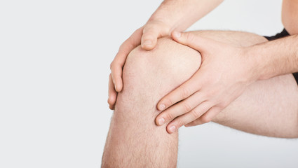 A man in underwear holds his knee with a hand on a gray background.