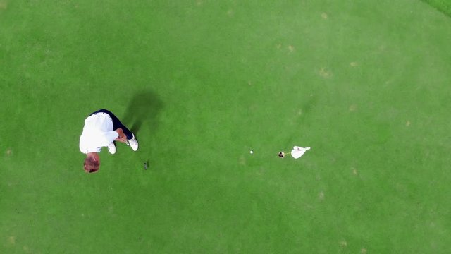 Person plays golf on a green course, putting a ball into hole.