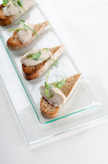 Bruschetta with liver pate and herbs on white table. Canape mini sandwiches Isolated on background. Banquet service with different food snacks and appetizers. Catering food, snacks. Party food.