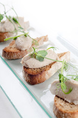 Bruschetta with liver pate and herbs on white table. Canape mini sandwiches Isolated on background. Banquet service with different food snacks and appetizers. Catering food, snacks. Party food.