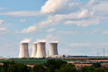 View of smoking chimneys of nuclear power plant, power lines and forest, under blue sky with clouds