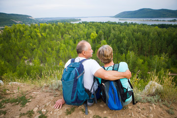 elderly couple with backpacks sits on the mountain. Senior couple walking in nature. travel tourism concept