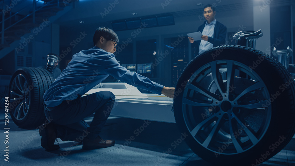 Wall mural team of automotive engineers working on electric car platform chassis, taking measures, working with