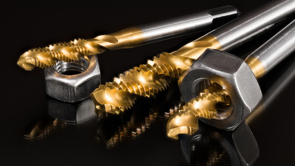 Titanium coated spiral flute taps and threaded nuts on black background. Artistic still life of...