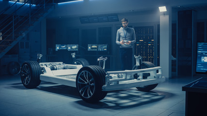 Automobile Engineer Working on Electric Car Platform Chassis Prototype, Using Tablet Computer with...