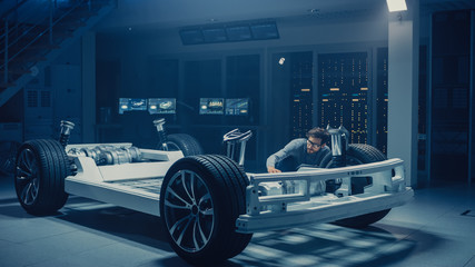 Automobile Engineer Working on Electric Car Platform Chassis Prototype, Using Tablet Computer with...