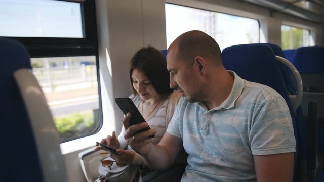 A couple in love sitting in comfortable chairs looking at the photos on the smartphone. A couple in love traveling in the elektro train looking through the window at the surroundings.