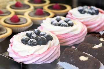 White pink meringue with blueberries, chocolate tartles with raspberries, other desserts on shelf in candy store. Close-up