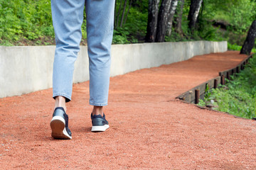 Obraz premium Woman legs walking on red gravel road in summer park. Outdoor sport, walking concept. Close-up, copy space