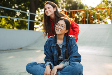 Image of two pretty girls laughing and riding skateboard together in skate park