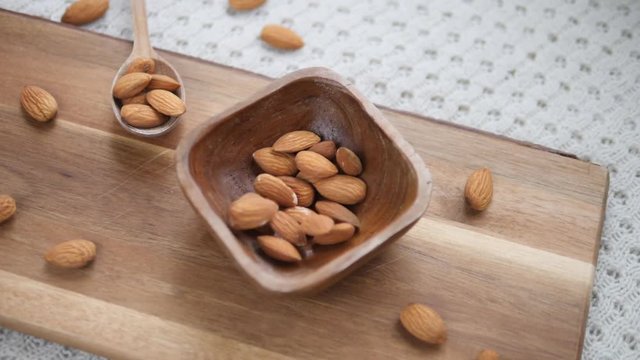 Top View Of Almonds On Wooden Board Falling In Wooden Bowl. Slow Motion.