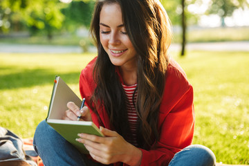 Fototapeta premium Image closeup of smiling girl student listening music with headphones while sitting in green park