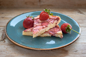 Piece of round strawberry berries tart pie pudding on blue plate on rustic wooden background