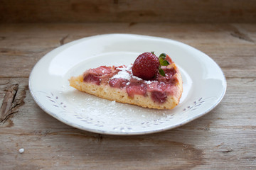 Piece of round strawberry berries tart pie pudding on white plate on rustic wooden background