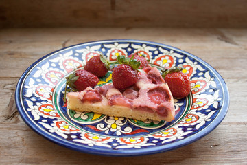 Piece of round strawberry berries tart pie pudding on plate with blue pattern on rustic wooden background