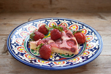 Piece of round strawberry berries tart pie pudding on plate with blue pattern on rustic wooden background