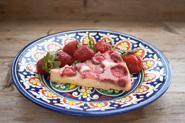 Piece of round strawberry berries tart pie pudding on plate with blue pattern on rustic wooden background