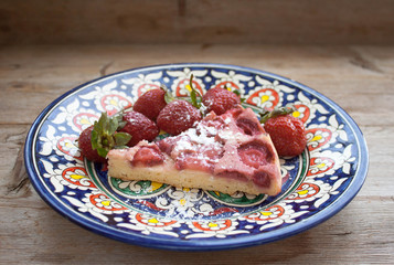 Piece of round strawberry berries tart pie pudding on plate with blue pattern on rustic wooden background